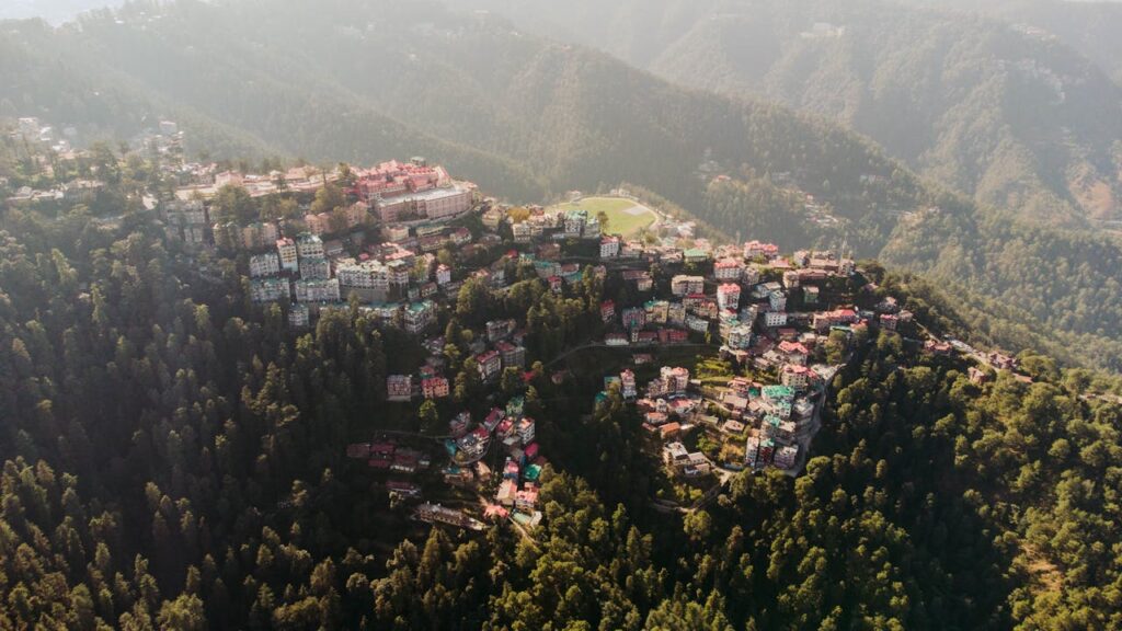 Aerial view of a city featuring numerous buildings, surrounded by mountains and fog with trees in the landscape.