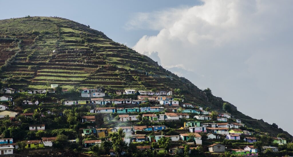 A scenic view of a town situated on a hill, surrounded by lush greenery and trees, with houses scattered among the landscape.